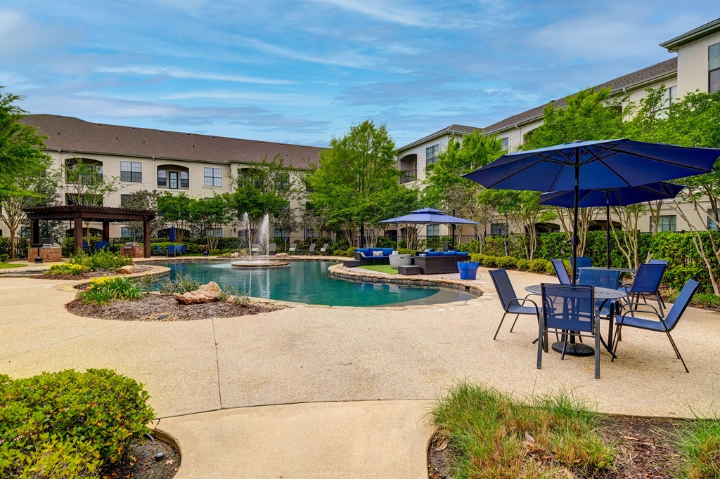 A pool area with a fountain, chairs, and umbrellas.